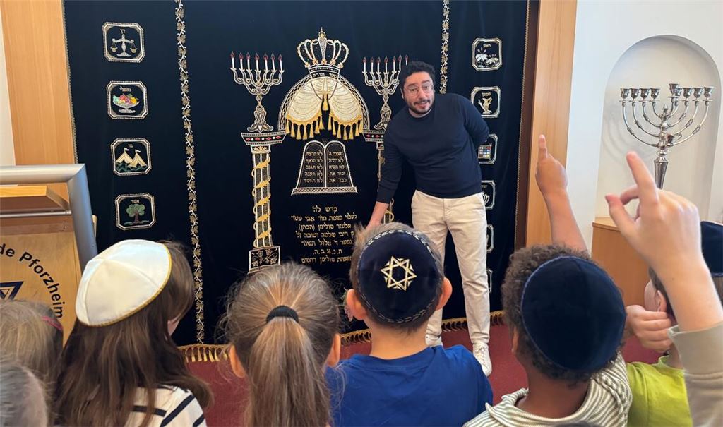 Hinter dem blauen Vorhang verbergen sich die Heiligtümer der Synagoge: Michael Suliman erklärt den Kindern, was es mit den Tora-Rollen auf sich hat. Fotos: Klassen