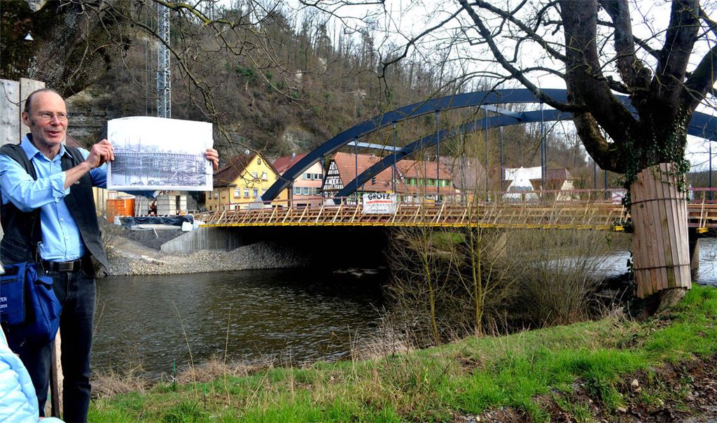 Historie und Gegenwart: Bei einer Führung mit Manfred Rapp – hier mit einem Foto vom Vorgängermodell des heutigen Bauwerks, im Hintergrund die künftige neue Herrenwaagbrücke, die ab April freigegeben werden soll – erhalten die Teilnehmerinnen und Teilnehmer Einblicke in die lange Geschichte der Enzübergänge in Mühlacker.Fotos: Stahlfeld