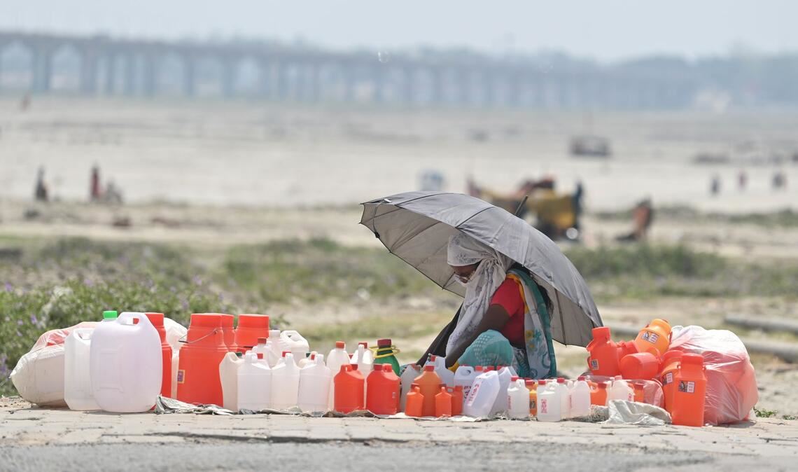 Hitze in Indien: Von Kanistern umgeben wartet ein Verkäufer mit einem Schirm in Prayagraj auf Kunden.
