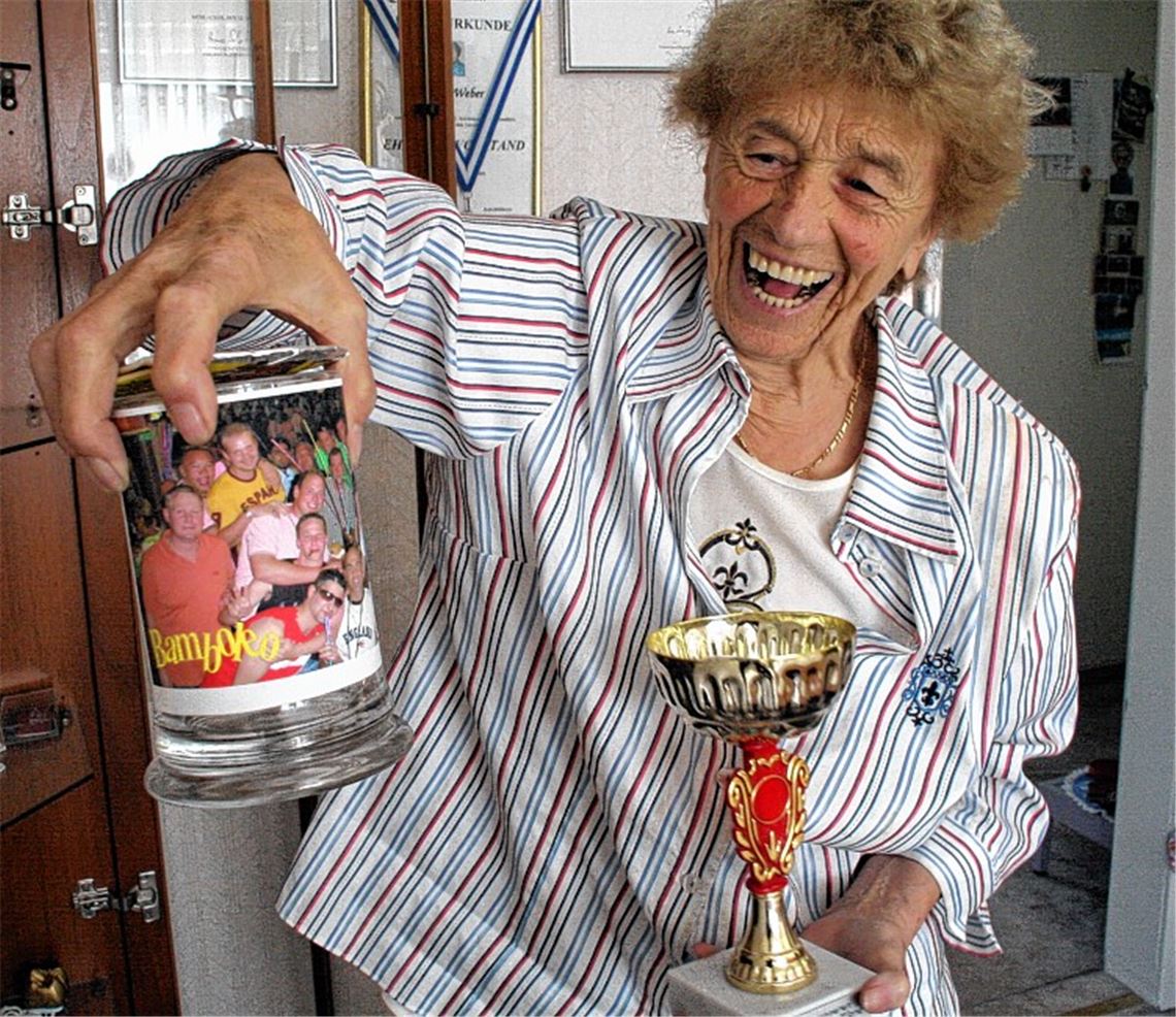 Ihr herzhaftes Lachen ist das Markenzeichen von Klara Weber, die stolz ein paar Geschenke ihrer Sportfreunde zeigt: einen Pokal mit Inschrift „Für unseren treuen Fan Klara“ und einen Bierkrug mit einem lustigen Mannschaftsfoto. Fotos: Eigner