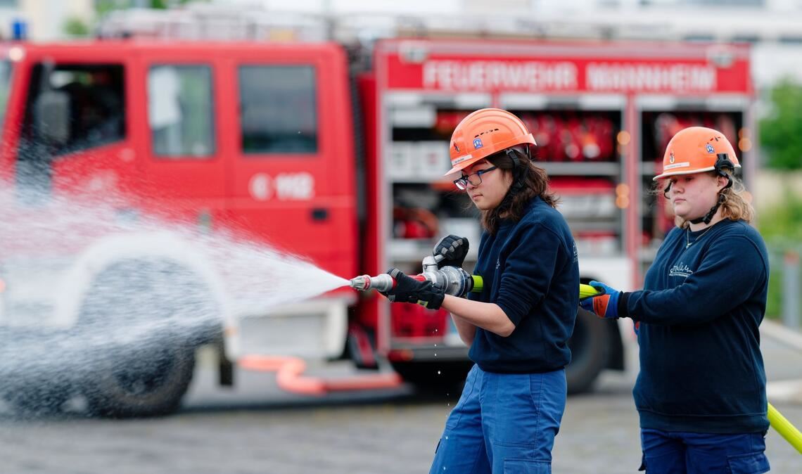 Ilias (links) und Annabella, Mitglieder der Jugendfeuerwehr in Mannheim, halten bei einer Übung einen Feuerwehrschlauch in den Händen.
