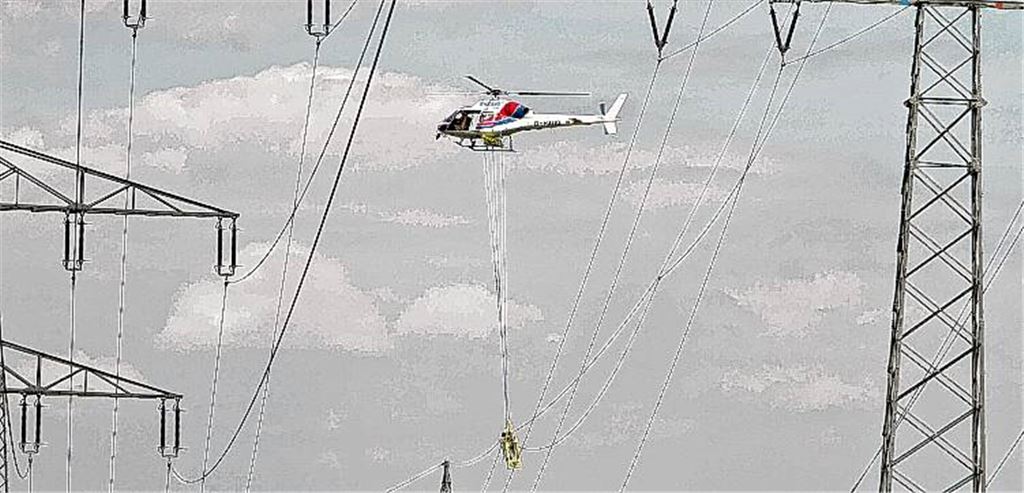 In dem Arbeitskorb unterhalb des Hubschraubers stehen Monteure, die die Hochspannungsleitungen in der Umgebung von Enzberg reparieren.Foto: Tilo Keller