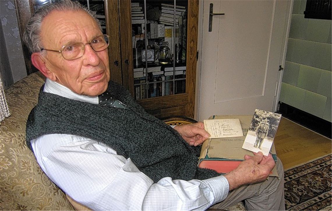 Ingo Daur mit einem dicken Buch zum Ersten Weltkrieg, einem Bild seines Vaters in Uniform und der ersten Postkarte, die dieser Monate nach seiner schweren Verwundung nach Hause schickte.