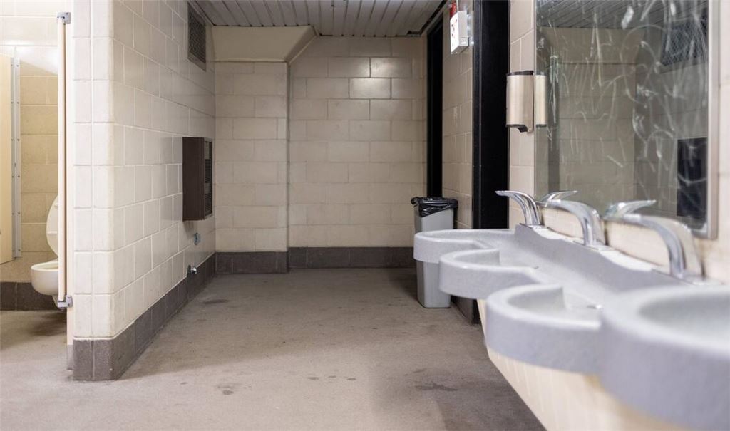 Innenansicht einer öffentlichen Toilettenanlage mit Waschbecken, Urinalen und einzelnen WC-Kabinen. Der Raum ist funktional gestaltet mit Fliesenwänden, Trennwänden und standardisierten Sanitäranlagen. Mulmig ist es einem trotzdem, wenn man an einem solchen Ort muss.