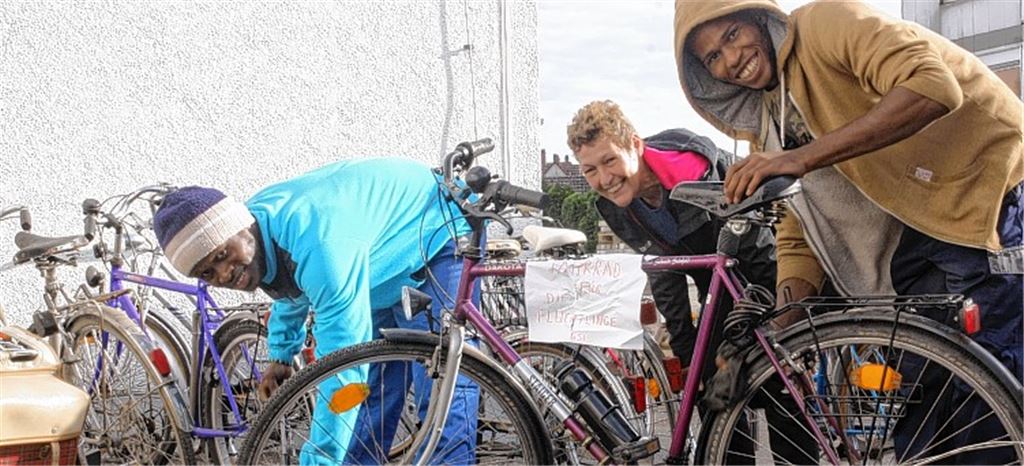 Ismael (li.) und Ibrahim (re.) packen mit an, um gespendete Fahrräder wieder flott zu machen. Mechthild Schwarz-Künkele (Mitte) ist begeistert von der Spendenzahl.