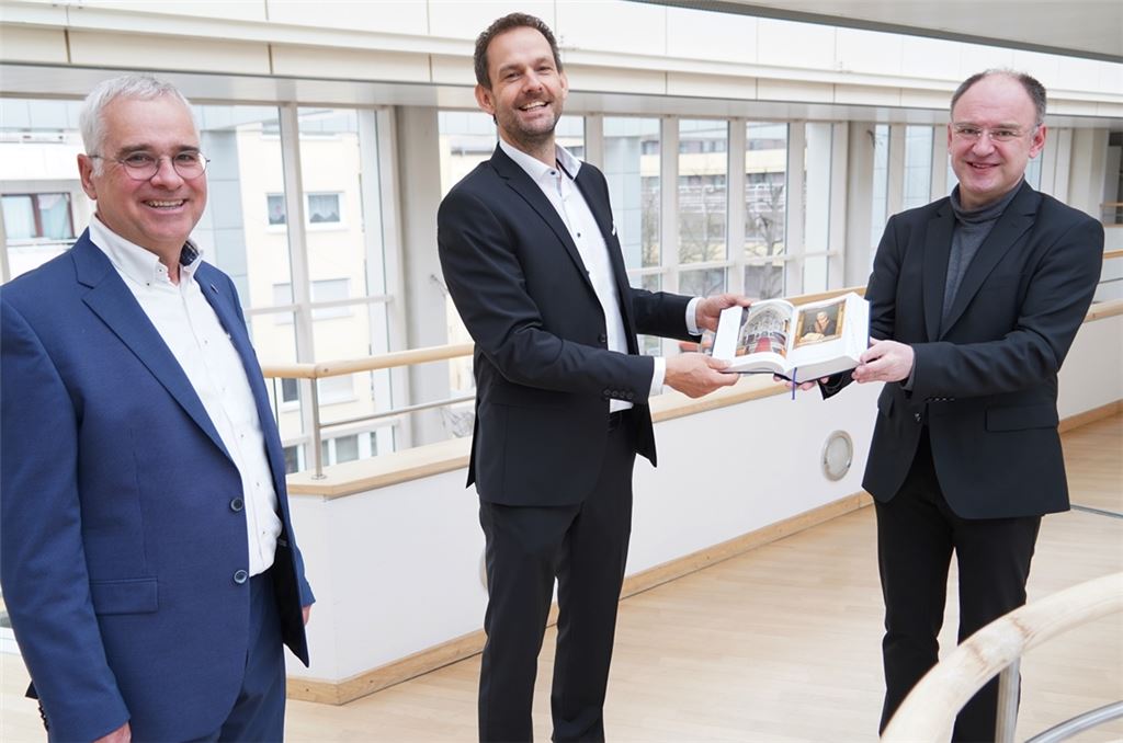 Jürgen Huber (li.) und Christoph Glimpel (re.) überreichen ein Exemplar der Enzkreis-Bibel an Landrat Rosenau. Foto: Roller