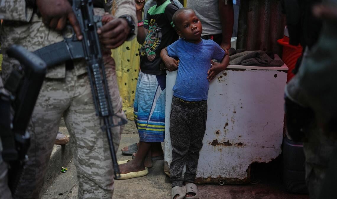 Kind neben bewaffnetem Polizisten in Unterkunft für Vertriebene in Port-au-Prince