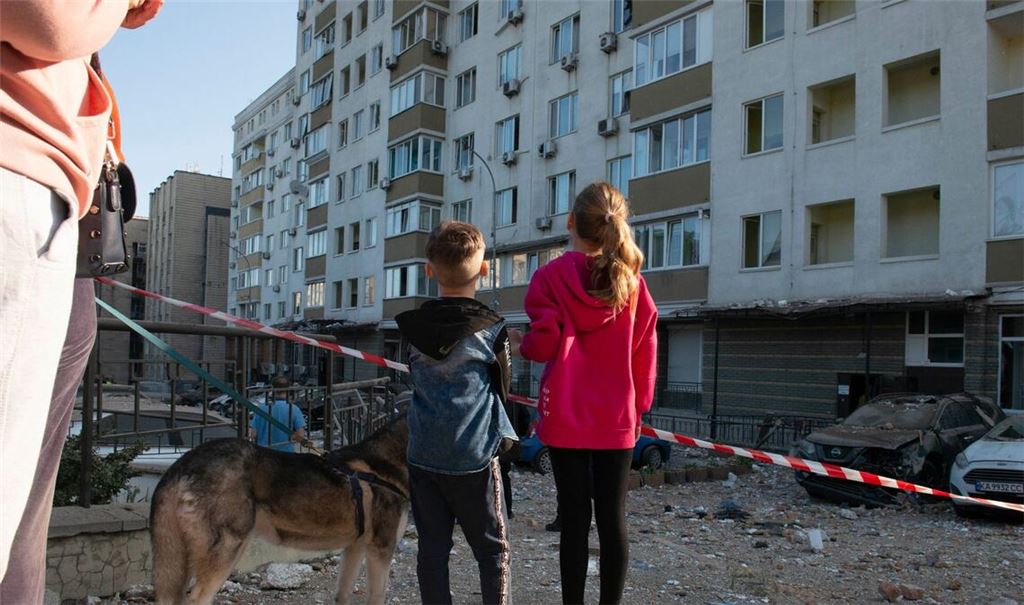 Kriegsalltag: Kinder schauen in Kiew auf ein bei russischen Raketenangriffen beschädigtes Gebäude.