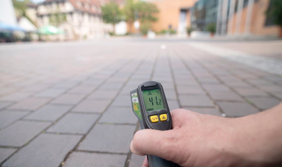 Kurz sorgt eine Wolke für Schatten auf dem Kelterplatz vor dem Rathaus. Trotzdem misst die Infrarotpistole eine Temperatur von über 41 Grad auf dem Pflaster. Fotos: Fotomoment