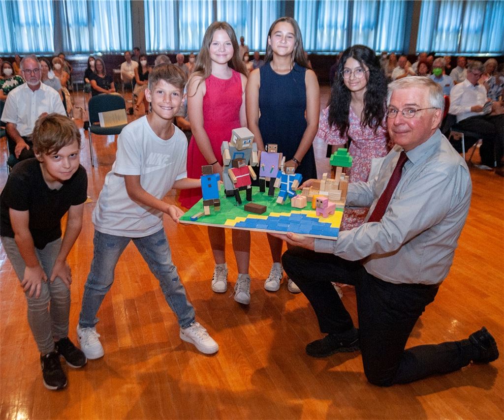 Lobende und dankende Worte zum Abschied: In einer Feierstunde haben viele Wegbegleiter den scheidenden Illinger Schulleiter Andreas Petermann für sein unermüdliches Engagement gelobt. Zu denen, die Danke gesagt haben, gehört auch die „Minecraft“-Gruppe der Schule. Die Fünft- und Sechsklässler Marco, Donik, Lilith, Mia und Mouna überreichen eine Bastelarbeit.Foto: Fotomoment