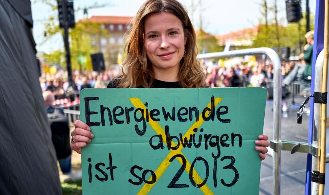 Luisa Neubauer hält ein Schild mit der Aufschrift "Energiewende abwürgen ist so 2013" in der Hand.