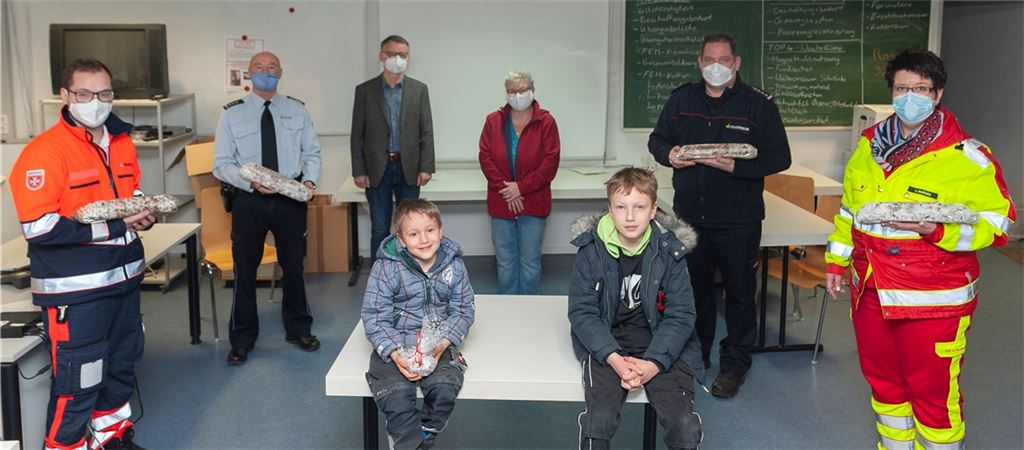Manuel und Maximilian Oser (sitzend) übergaben Christstollen an Quentin Joos (Rettungssanitäter) und Frank Krebs, Leiter Polizeirevier Mühlacker (von links) sowie Irmgard Jedlicka und Matthias Donath (von rechts), denen Michael Rieger und Gisela Oser von der Verkehrswacht dankten. Foto: Fotomoment