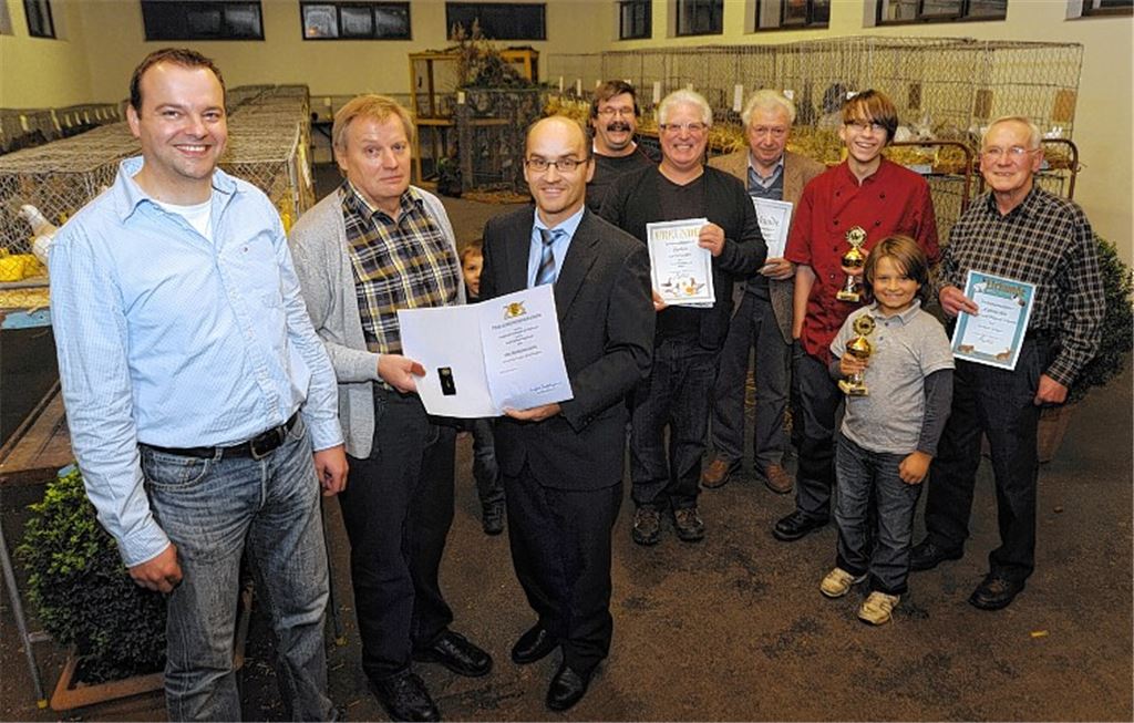 Marco Mannhardt, der Erste Vorsitzende des Kleintierzuchtverein Illingen, strahlt bei der Verleihung der Landesehrennadel an Norbert Mannhardt durch lllingens Bürgermeister Harald Eiberger (v. li.) bei der Lokalschau, in deren Rahmen die aktuellen Vereins- und Jugendmeister (rechts hinten im Bild ) Urkunden und Pokale erhalten haben.
