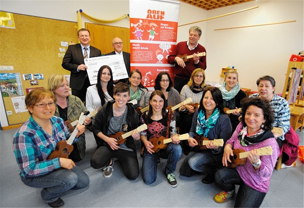Marktdirektor Gerd Owczarek von der Sparkasse übergibt 3000 Euro an Helmut Wagner (hinten v. li) für das Ukulele-Projekt von ObenAuf, bei dem in Enzberg 14 Erzieherinnen auf dem Zupfinstrument von Sebastian Weber (hinten re.) unterrichtet werden. Foto: Fotomoment