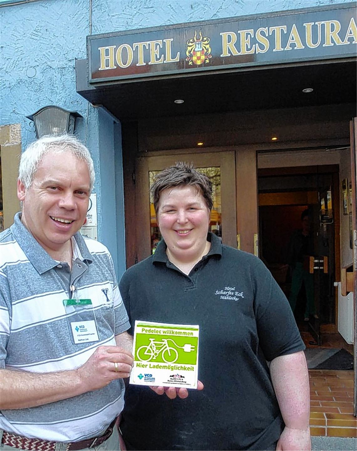 Matthias Lieb vom Verkehrsclub Deutschland übergibt „Pedelec Willkommen“-Aufkleber an Karin Frommherz vom „Scharfen Eck“. Foto: privat