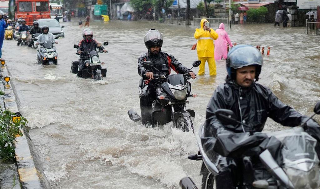 Menschen fahren bei starkem Regen in Mumbai mit Motorrädern durch eine überschwemmte Straße.