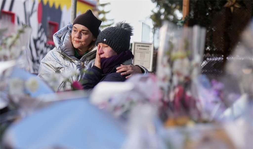 Menschen trauern hinter Blumen und Briefen in der Nähe der abgeriegelten Le Constellation Bar, wo ein verheerender Brand während der Neujahrsfeierlichkeiten Tote und Verletzte forderte.