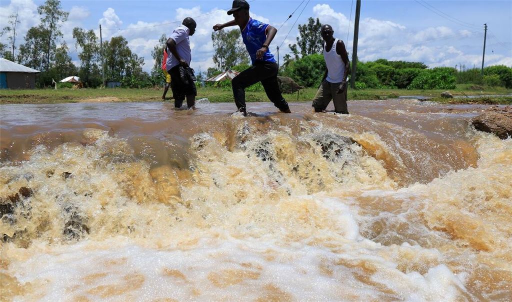 Menschen überqueren einen überfluteten Straßenabschnitt nach schweren Regenfällen in Ahero, Kenia.