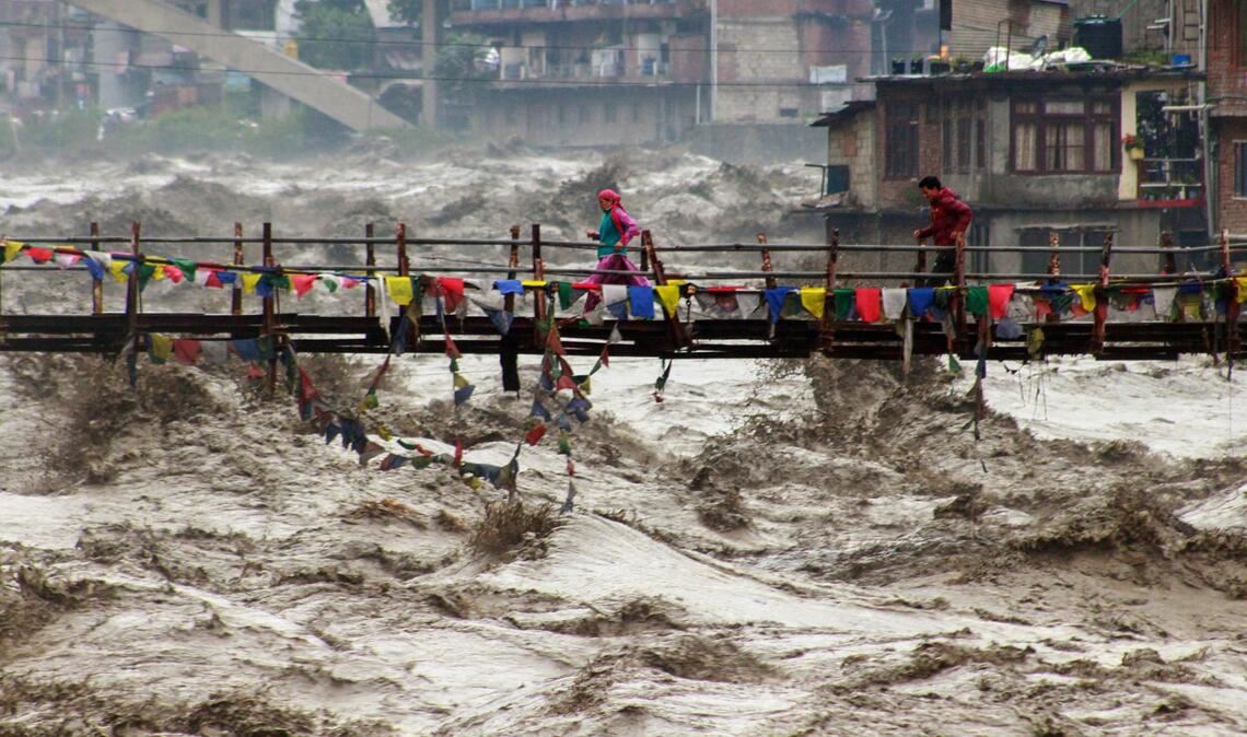 Menschen wagen im nordindischen Bundesstaat Himachal Pradesh trotz schwerer Überschwemmungen den Weg über eine Brücke, um den Fluss Beas zu überqueren.