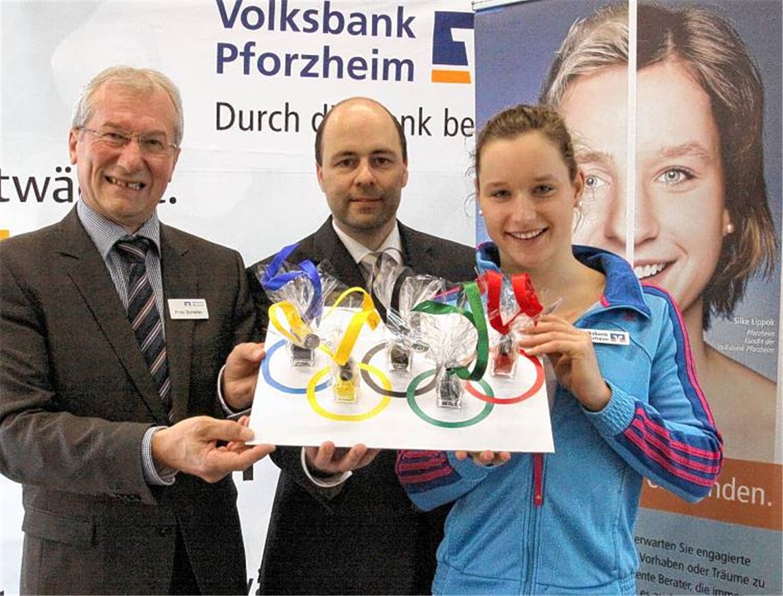 Mit Nagellack in den fünf olympischen Farben wünschen Fritz Schäfer (li.) und Ulf Lauche im Namen der Volksbank Pforzheim viel Glück für die Olympia-Qualifikation. Im Hintergrund lacht die Spitzenschwimmerin von einem Werbeplakat des Geldinstituts. Foto: Eigner