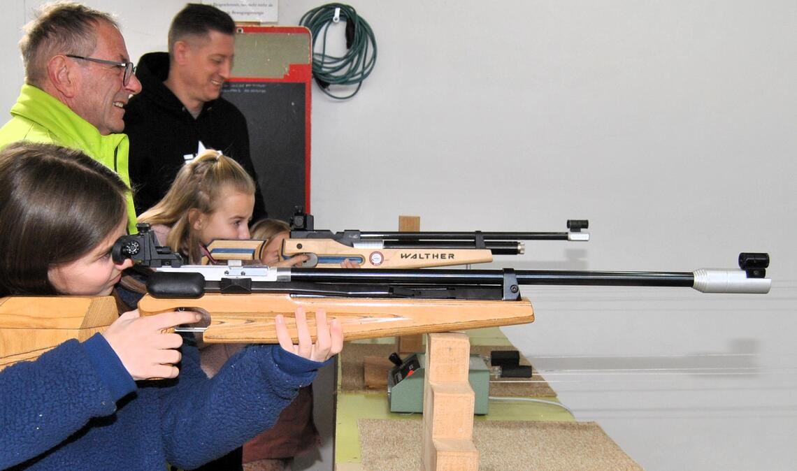 Mit dem Luftgewehr sichern sich Lilly (12) und Amelie (10, hi.) zur Freude von Oberschützenmeister Edgar Müller etliche bunt gefärbte Trophäen. Foto: Haller