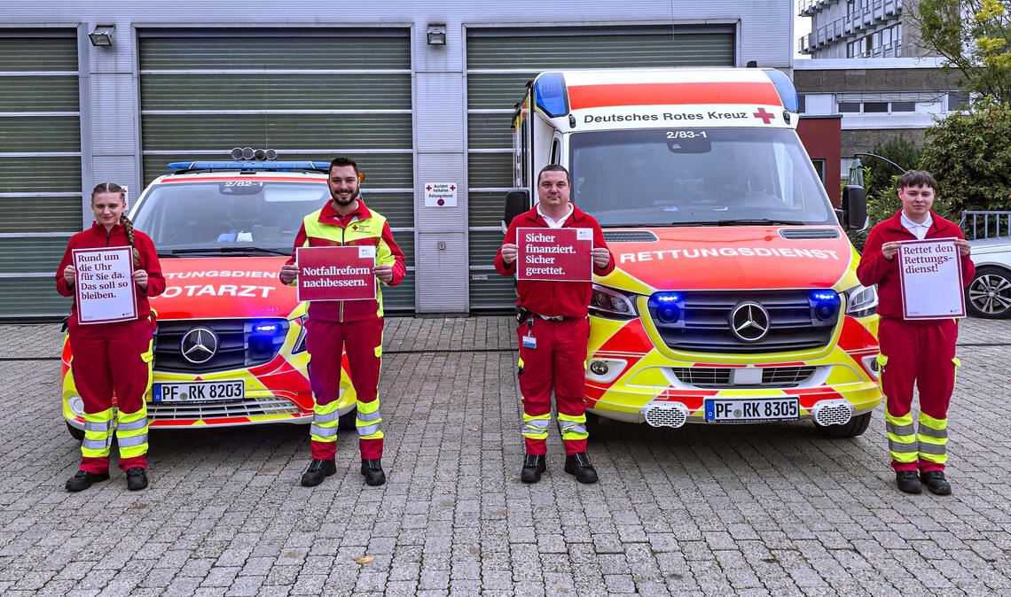 Mitglieder des DRK-Rettungsdienstes machen vor der Rettungswache 2 in Mühlacker mit Plakaten auf die Forderungen nach einer verlässlichen und auskömmlichen Finanzierung des Rettungsdienstes aufmerksam (v.li.): Alena Gölz, Auszubildende zur Notfallsanitäterin, Jonas Kucher, Notfallsanitäter, Jörg Kriegisch, Rettungssanitäter und Wachenleiter, und Florian Engel, Notfallsanitäter. Foto: Anna Brenner/DRK Pforzheim-Enzkreis e. V.