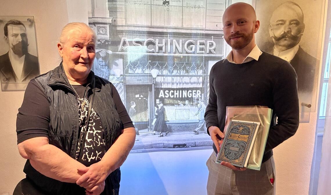 Monika Dreher geborene Aschinger mit Stadtarchivar Marco Rödler. Im Hintergrund sind die Porträts von Karl und August Aschinger zu sehen und ein Mitte der 1930er Jahre entstandenes Bild des Lokals an der Leipziger Straße 79 in Berlin. Foto: Jürgen Dreher