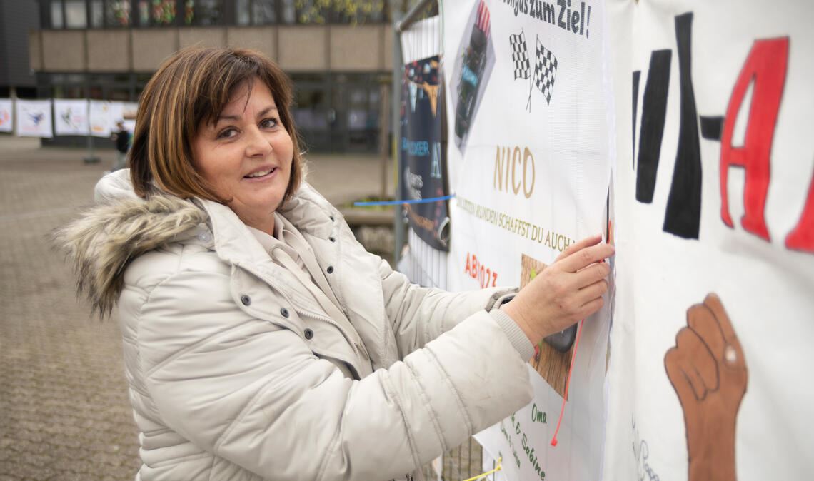 Mutter Marion König befestigt ein Plakat für ihren vor dem Abitur stehenden Sohn Nico an einem zu diesem Zweck aufgestellten Bauzaun. Foto: Fotomoment