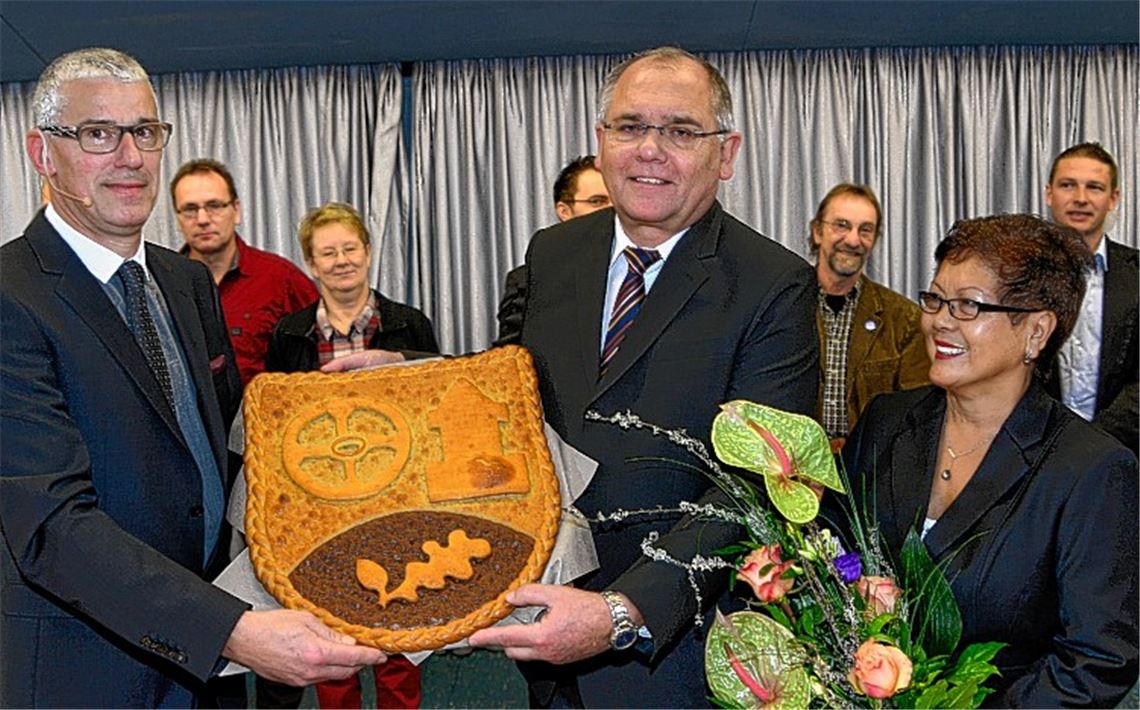 Nach der Verpflichtung: Helmut Schneider (li.) überreicht Norbert Holme ein von der Bäckerei Scheytt gebackenes Gemeindewappen und an Ehefrau Lily Holme einen Blumenstrauß.