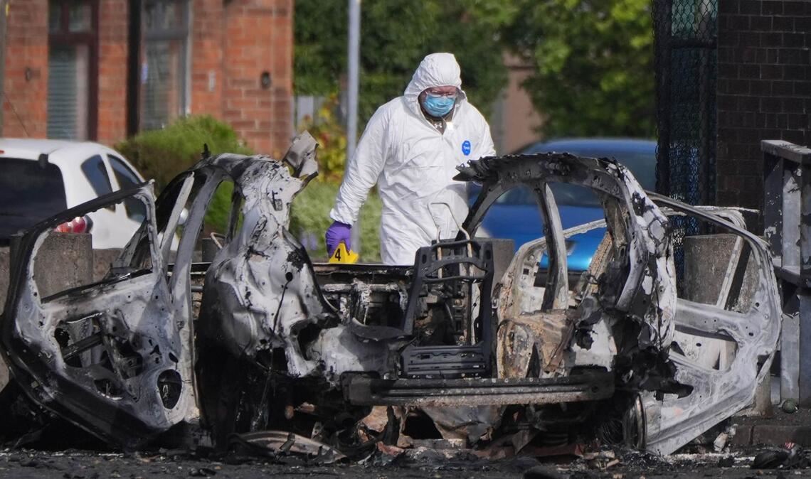 Nach einer Explosion vor einer Polizeistation steht ein Ermittler neben einem zerstörten Auto in Dunmurry, nahe Belfast in Nordirland.