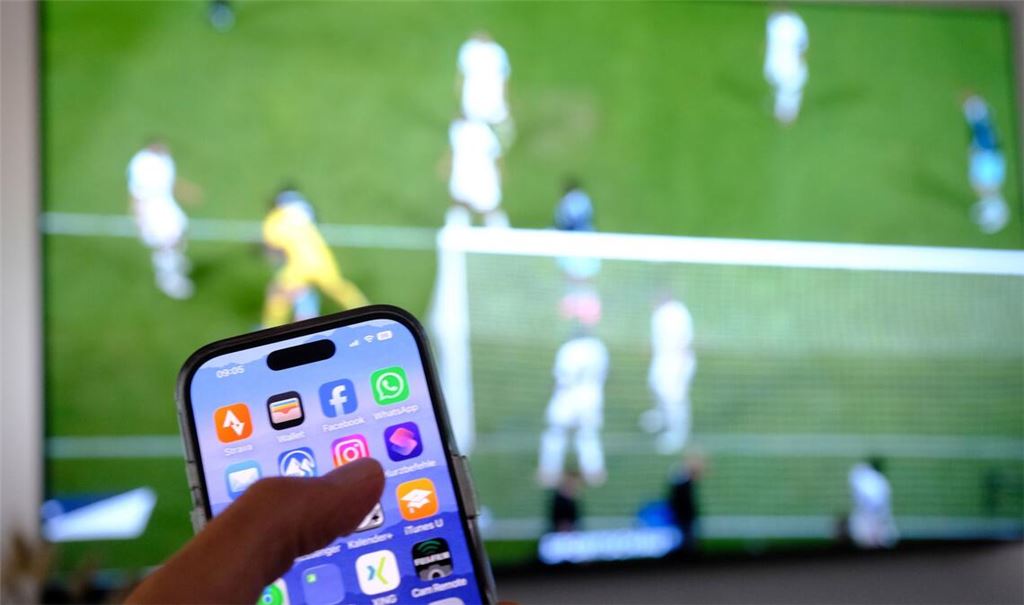 Nebenbei mal daddeln: Während das Fußballspiel läuft, schauen viele Zuschauer nebenbei aufs Handy. (Symbolbild)