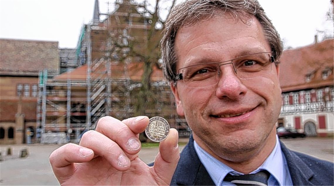 „Nettes Schmankerl“: Der Maulbronner Bürgermeister Andreas Felchle freut sich über die neue Zwei-Euro-Münze mit Maulbronner Motiv. Im Hintergrund ist die derzeit eingerüstete Fassade der Klosterkirche zu sehen, die für das Geldstück Modell stand. Neben der Westfassade des Gotteshauses mit dem Paradies ist auf das Zahlungsmittel noch der dreischalige Brunnen des Kreuzgangs geprägt. 
