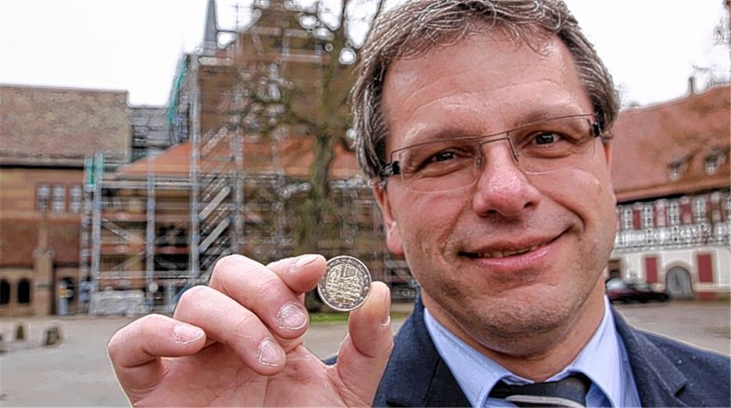 „Nettes Schmankerl“: Der Maulbronner Bürgermeister Andreas Felchle freut sich über die neue Zwei-Euro-Münze mit Maulbronner Motiv. Im Hintergrund ist die derzeit eingerüstete Fassade der Klosterkirche zu sehen, die für das Geldstück Modell stand. Neben der Westfassade des Gotteshauses mit dem Paradies ist auf das Zahlungsmittel noch der dreischalige Brunnen des Kreuzgangs geprägt. 