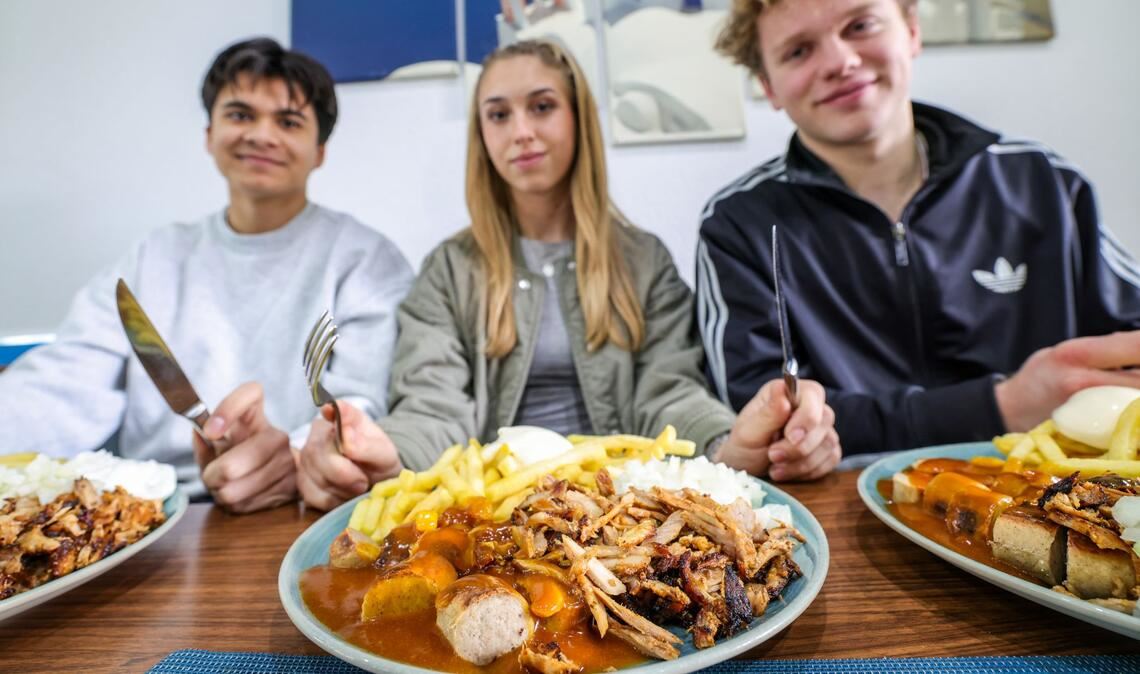 Nickolas Krugmann (li.-re.), Antonija Dreznjak und Lukas Kampen sitzen vor ihren „Taxi-Tellern“ in einem Imbiss. Pommes, Currywurst und dazu massenweise Gyros mit Zwiebeln: Im Ruhrgebiet sorgt der Taxi-Teller für Begeisterung bei Fast-Food-Fans. Das Gericht ist länger bekannt, neuerdings aber voll im Trend.