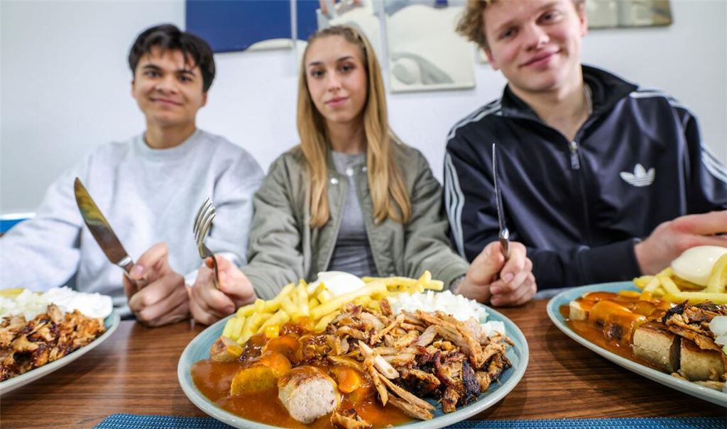 Nickolas Krugmann (li.-re.), Antonija Dreznjak und Lukas Kampen sitzen vor ihren „Taxi-Tellern“ in einem Imbiss. Pommes, Currywurst und dazu massenweise Gyros mit Zwiebeln: Im Ruhrgebiet sorgt der Taxi-Teller für Begeisterung bei Fast-Food-Fans. Das Gericht ist länger bekannt, neuerdings aber voll im Trend.
