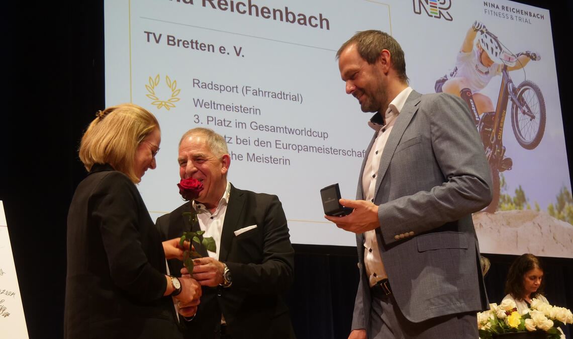 Nina Reichenbach wird von Henry Wiedemann, dem Vorsitzender des Sportkreis Pforzheim-Enz (Mi.) und Landrat Bastian Rosenau ausgezeichnet (linkes Bild).