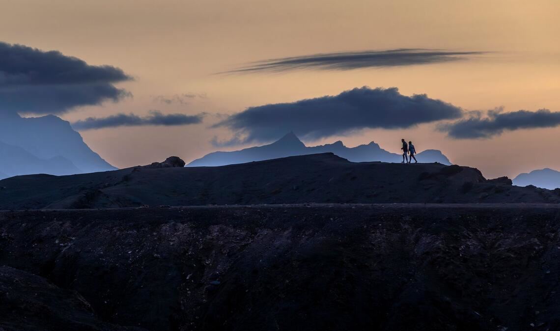 Panodrama: Menschen gehen auf der Insel Fuerteventura unter dramatisch wirkenden Wolkenformationen.