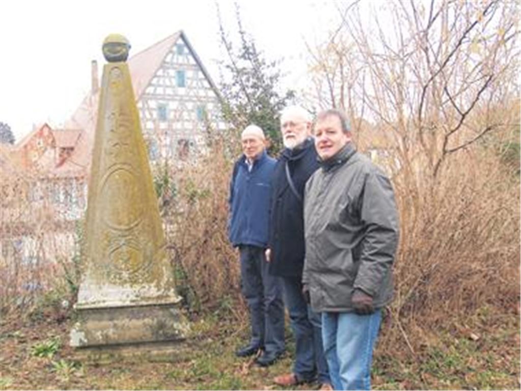 Pfarrer Beatus Widmann, Fotograf Manfred Läkemäker und Wolfgang Rieger vom Historisch-Archäologischen Verein (v.re.) vor dem ältesten Grabstein auf dem Dürrmenzer Friedhof. Hier hat Rosina Zeller, geb. Klemm, 1795 ihre letzte Ruhestätte gefunden. Im Hintergrund: das Dürrmenzer Pfarrhaus von 1699. 
Foto: Filitz