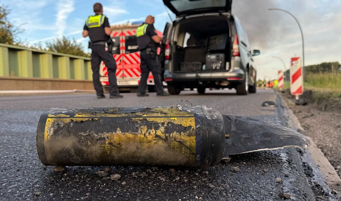 Polizisten stehen hinter einem Metallbehälter. Trümmerteile sollen bei dem Brand Hunderte Meter weit geflogen sein.