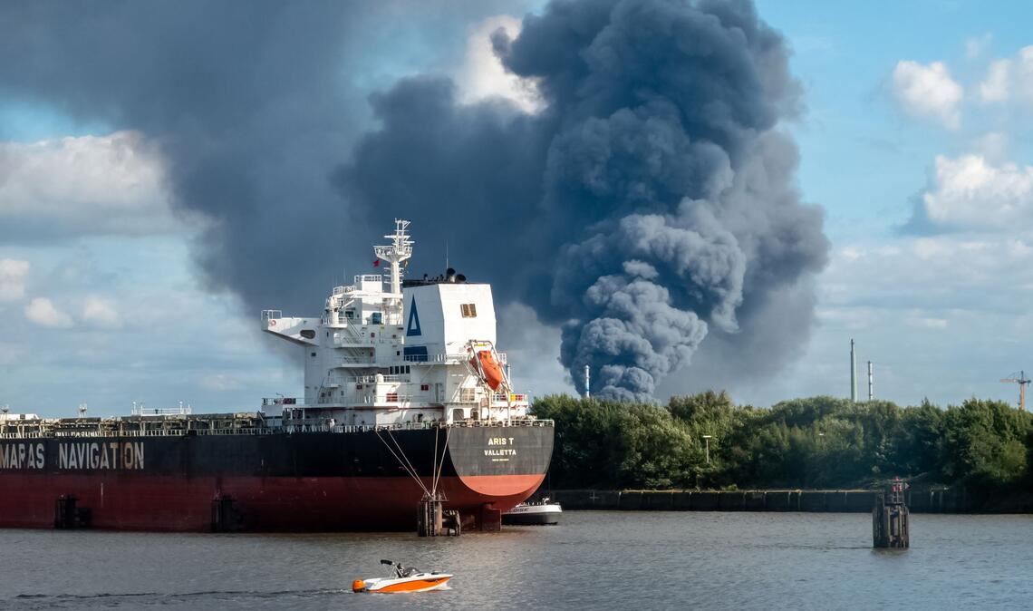 Rauch ist hinter einem Schiff zu sehen; in der Nähe des Einsatzortes fließt die Norderelbe.