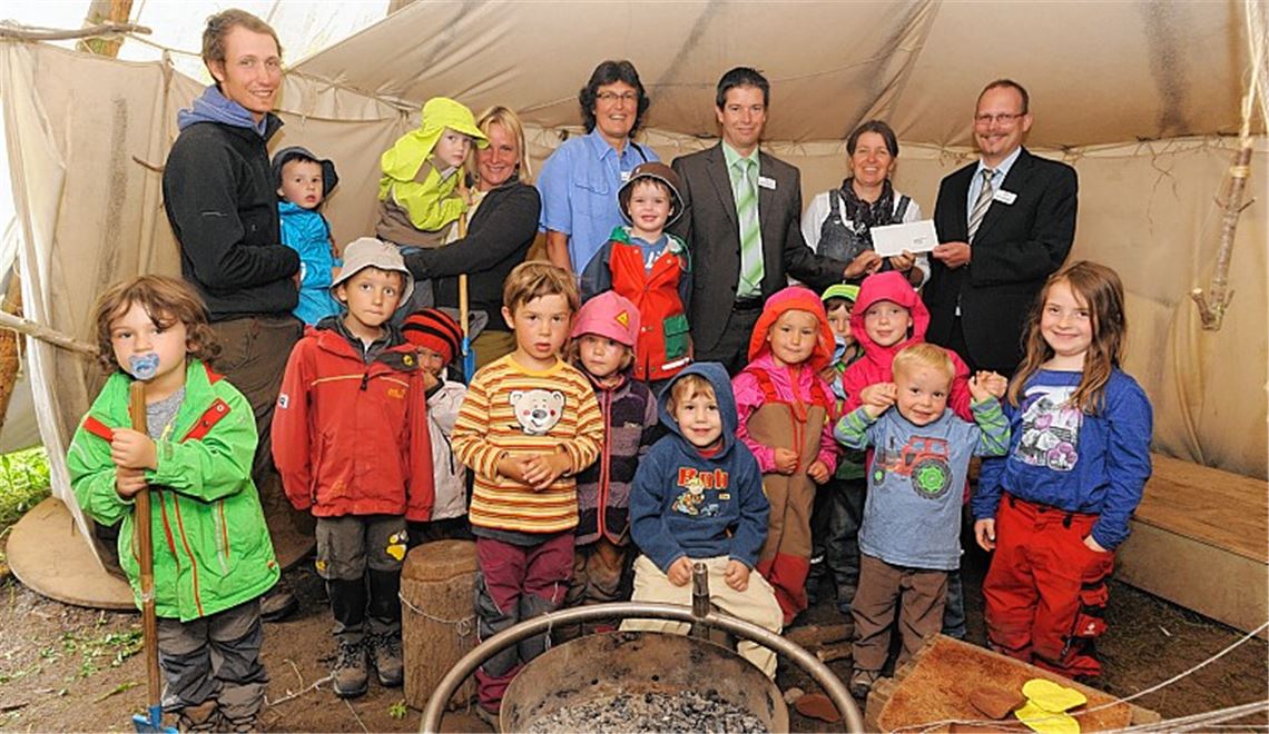 Regionalleiter Eric Großmann überreicht den Scheck an Sabine Pörner. Mit dabei sind Reinhold Baral und Susanne Kimmich, die Erzieherin Manuela Burkhard (hinten v.re.), ihr Kollege Daniel Siebert (hinten li.) und die Kinder, die sich über die Spende freuen.