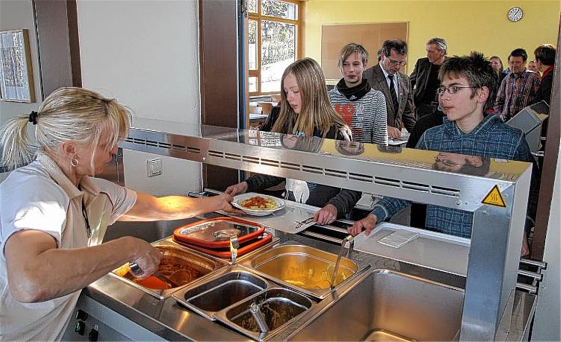 Schlange stehen bei der Premiere: Während die Schüler am ersten Tag an der neuen Essenausgabe auf Makkaroni setzen, greifen die erwachsenen Premierengäste wie der Bürgermeister eher zu den zünftigen Geflügelwürstchen mit Sauerkraut und Kartoffelbrei. 
