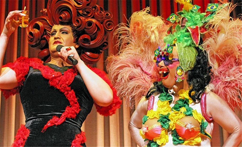 Schwester Bärbel als Copacabana-Schlampe kredenzt dem Travestie-Fräulein Wommy Wonder mit der Monsterperücke aus Isomatten-Streifen eine kühle Erfrischung. 