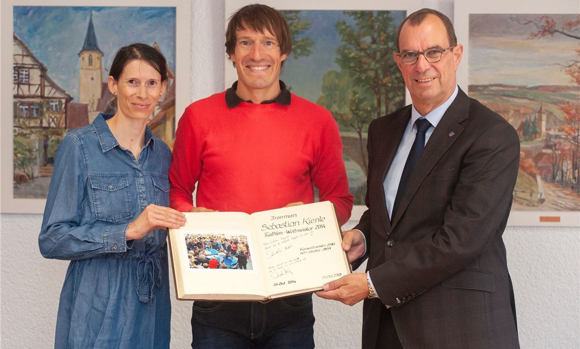 Sebastian Kienle mit dem Goldenen Buch und dem Eintrag zum Ironman-Sieg 2014, links seine Frau Christine Schleifer und rechts Oberbürgermeister Frank Schneider. Foto: Fotomoment