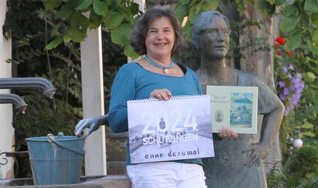 Selma Gienger zeigt am Brunnen, der einst ihrer Familie gehörte, ihren Kalender mit alten Bildern aus der Heimat und die Ortschronik ihres Vaters. Foto: Goertz