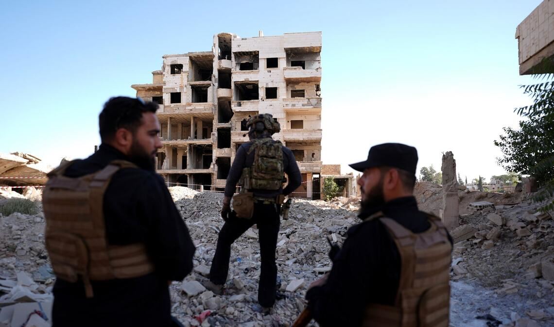 Sicherheitskräfte aus Syrien und aus Deutschland sichern den Besuch von Außenminister Wadephul bei einem humanitären Projekt in einer Straße mit während des Bürgerkriegs zerbombten Häusern in Harasta ab.