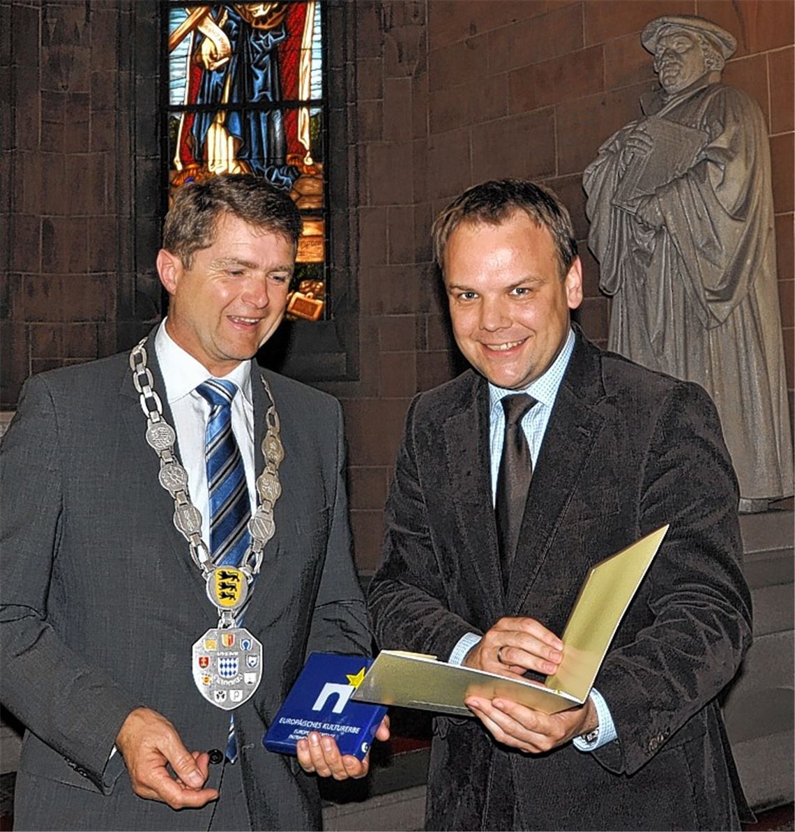 Staatssekretär Ingo Rust übergibt das Kulturerbe-Siegel an OB Martin Wolff (li.).