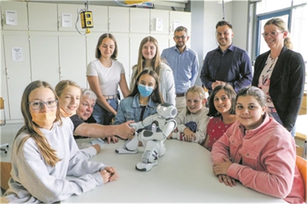 Stehend von rechts: Kerstin Weipert (WFG), René Baral und Kristofer Sperry (beide Nox Robots). In Aktion zu sehen ist Lehrer Klaus Gerlinger, der dem sozialen Roboter „Nao“ die Hand reicht, umringt von Teilnehmerinnen. Foto: Wewoda