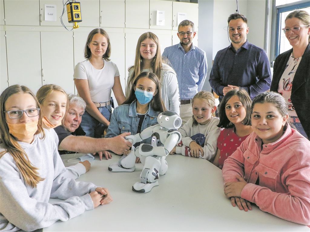 Stehend von rechts: Kerstin Weipert (WFG), René Baral und Kristofer Sperry (beide Nox Robots). In Aktion zu sehen ist Lehrer Klaus Gerlinger, der dem sozialen Roboter „Nao“ die Hand reicht, umringt von Teilnehmerinnen. Foto: Wewoda