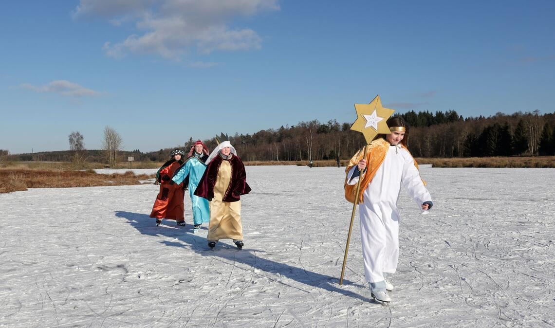 Sternsinger sind im Sonnenschein bei Betzenweiler in Tiefenbach mit Schlittschuhen auf einem zugefrorenen See unterwegs.